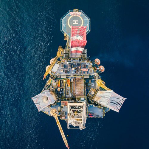High-angle view of an offshore oil platform with helipad surrounded by deep blue ocean.